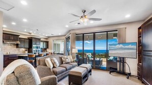 A spacious living area with a large sofa, a flat-screen TV, and a view of the ocean through large sliding doors. - ONE of Our BEST! Fresh Pricing, UPSCALE Renovations; (22V-1) where you get HUGE OCEAN Views (Lahaina)