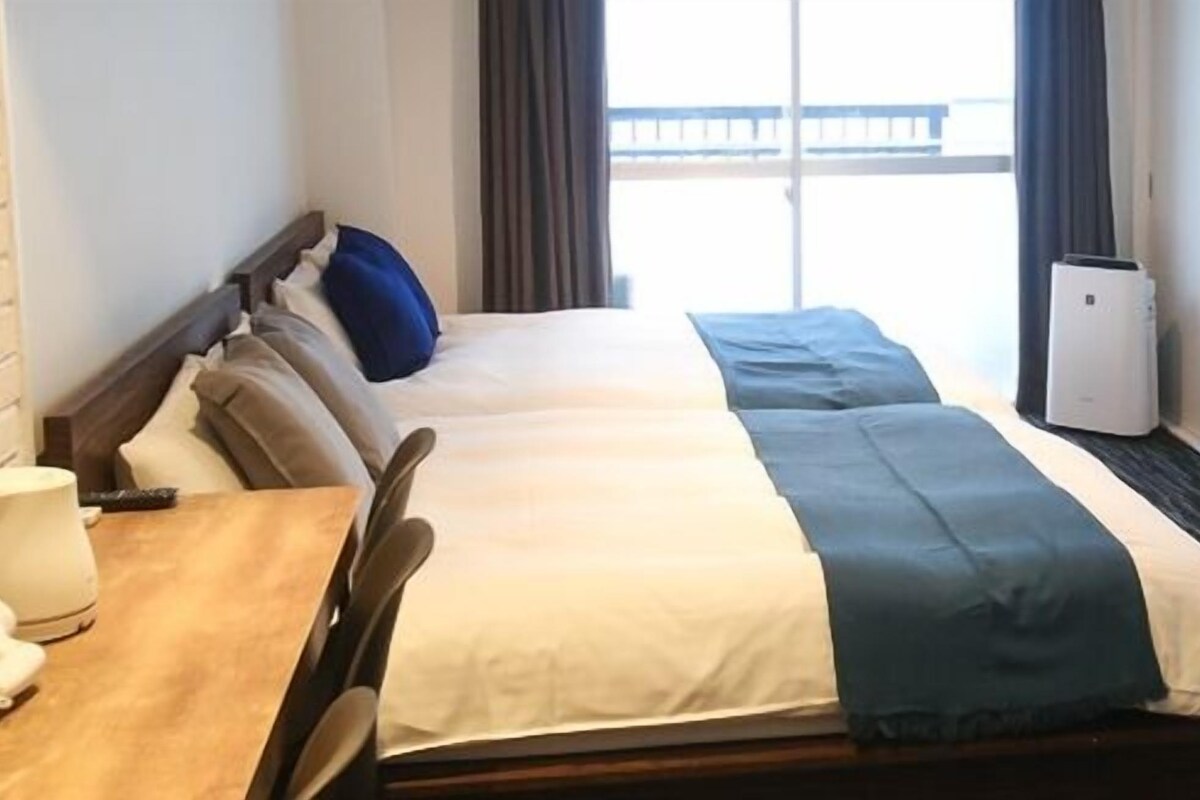 Une chambre d’hôtel avec un lit, une table avec une lampe, une télévision et une fenêtre avec des rideaux.