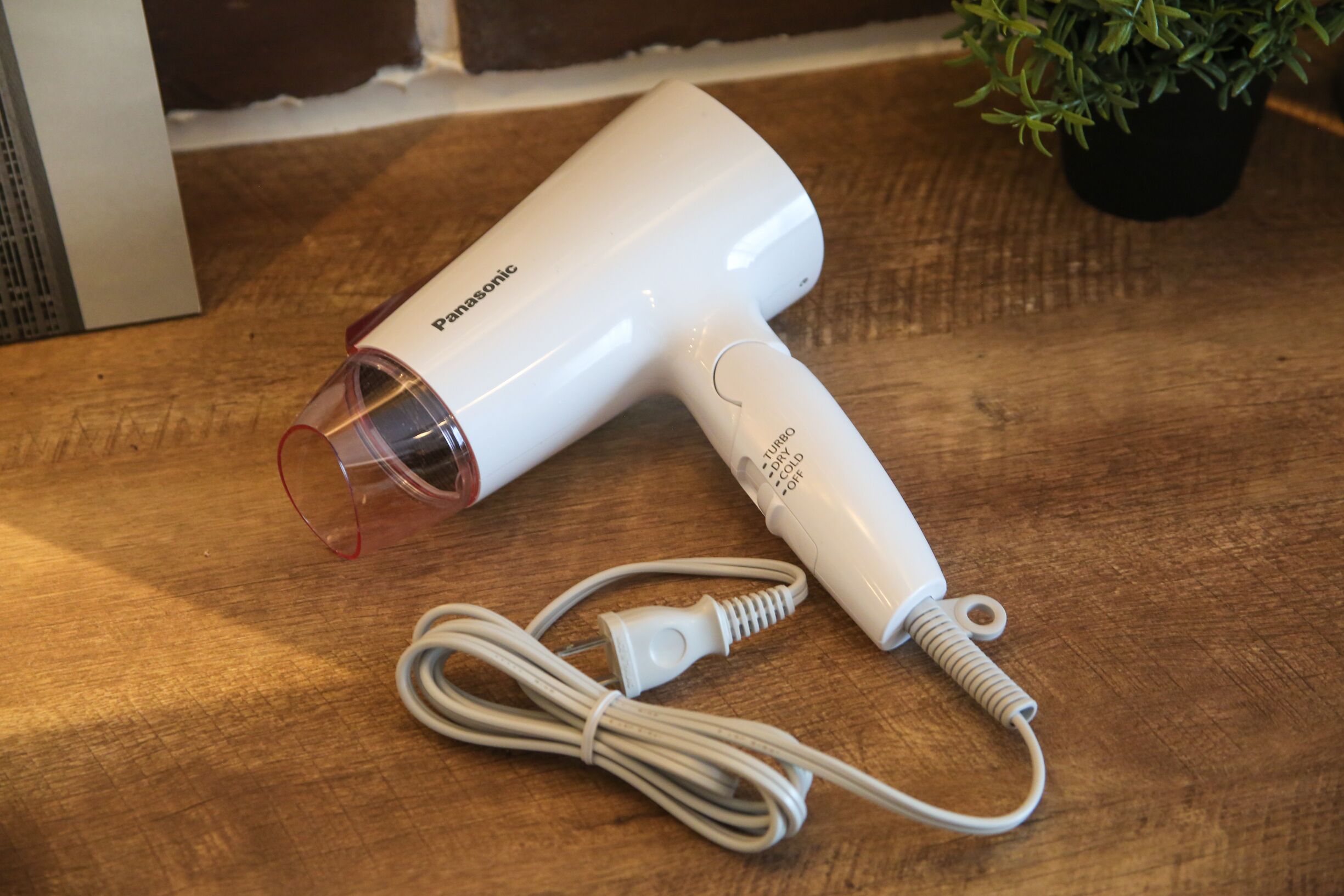 A Panasonic hair dryer with a red nozzle and a white cord on a wooden surface.