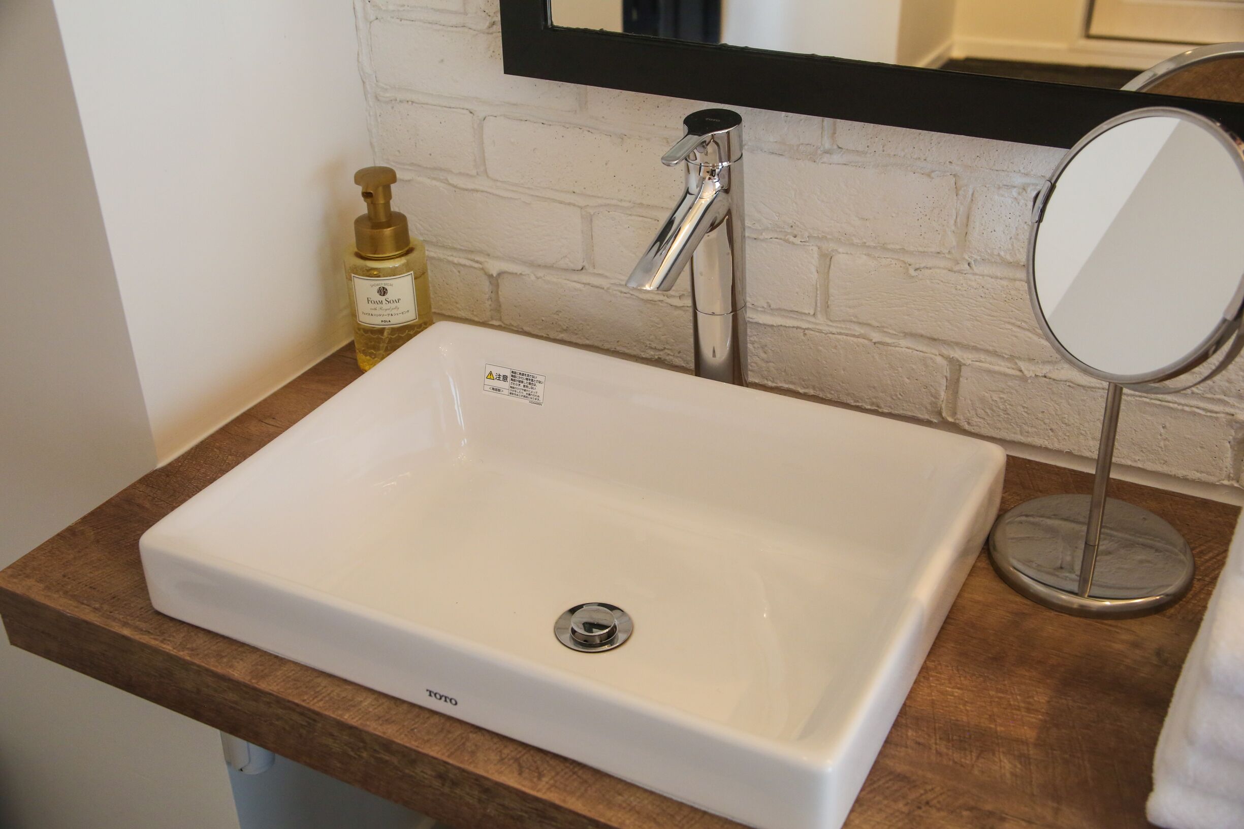 A bathroom with a white sink, a wooden countertop, a mirror, and a soap dispenser.