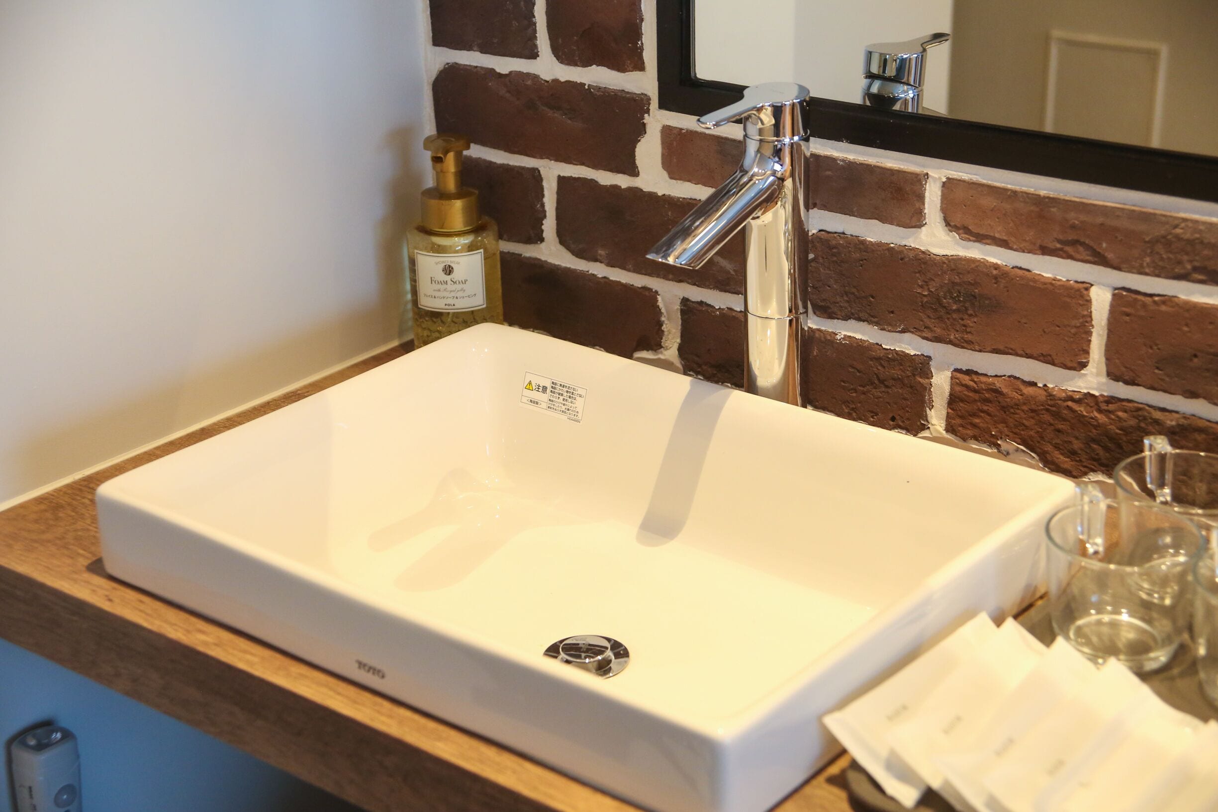 Un lavabo rectangular blanco con un grifo de cromo, un dispensador de jabón y un espejo encima.