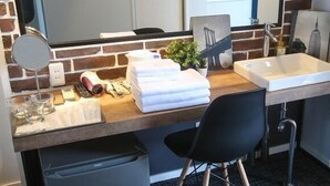Ein kleines Hotelzimmer mit Küchenzeile, einem Waschbecken, einem Spiegel und einem schwarzen Stuhl.