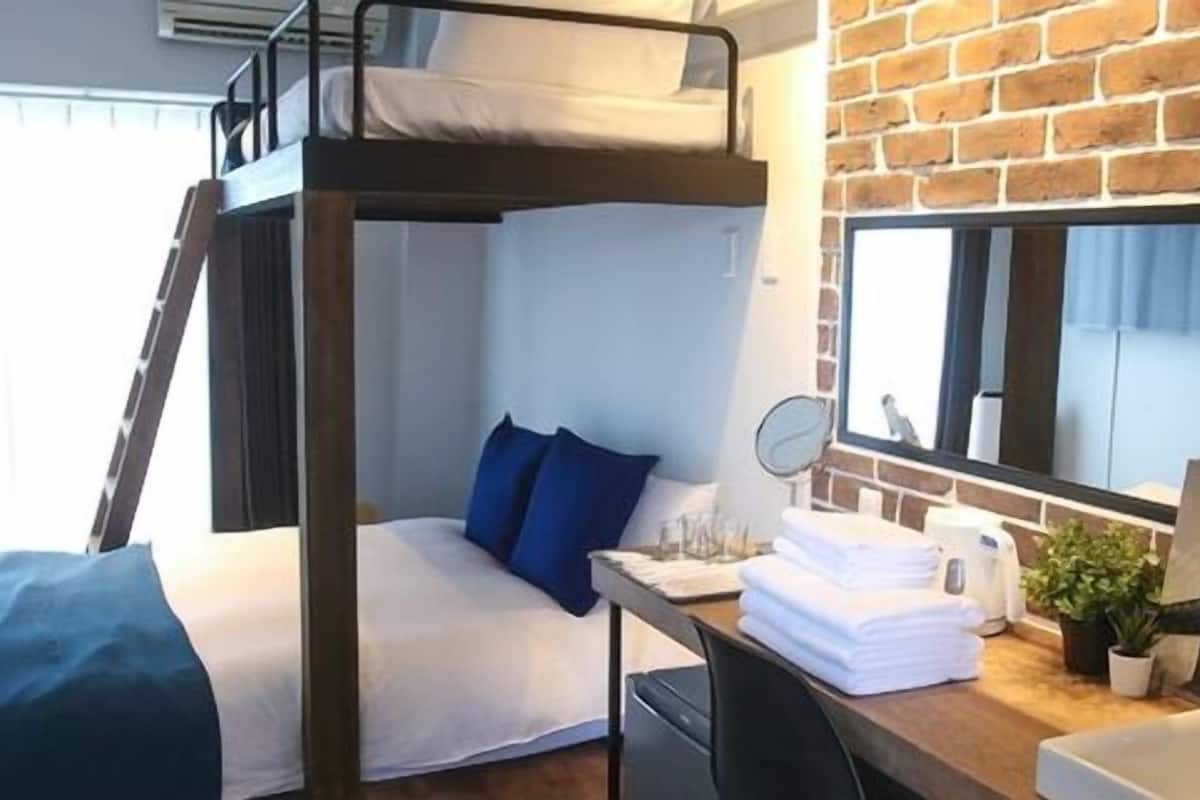 Een slaapkamer met een stapelbed, bureau, wastafel en spiegel.