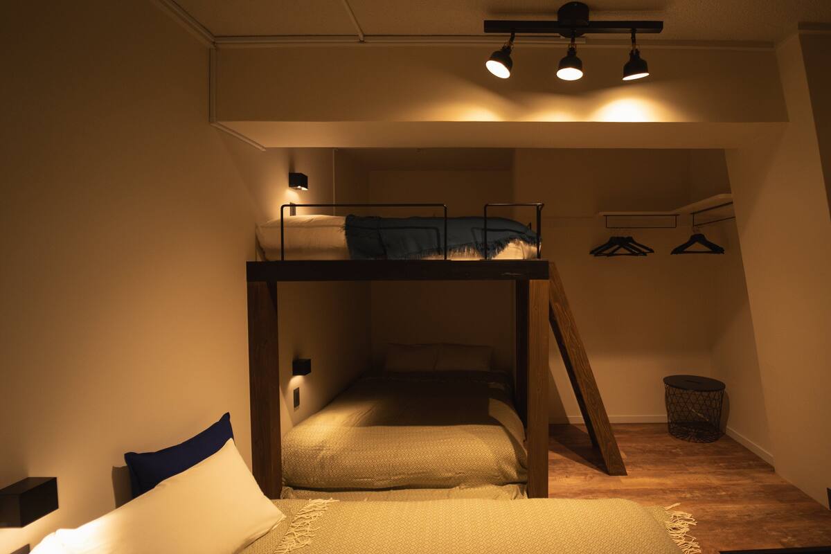Een slaapkamer met een stapelbed, een houten ladder, een klein tafeltje en een kledingrek.