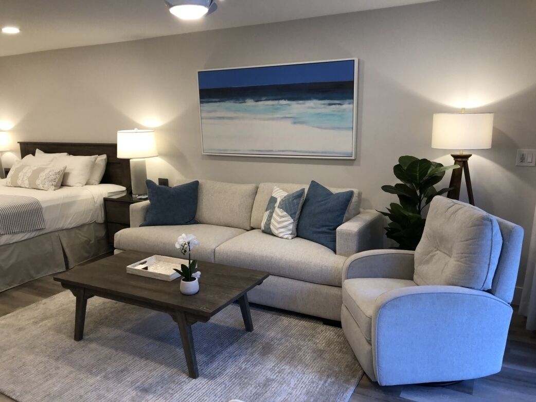 Un salon moderne avec un canapé, une table basse et un lit. Il y a un tableau au mur et une lampe sur la table d’appoint.