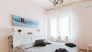 A neatly made bed with a patterned bedspread, a bedside lamp, and a wall-mounted painting of a bridge. - Acquadimare (Viareggio)