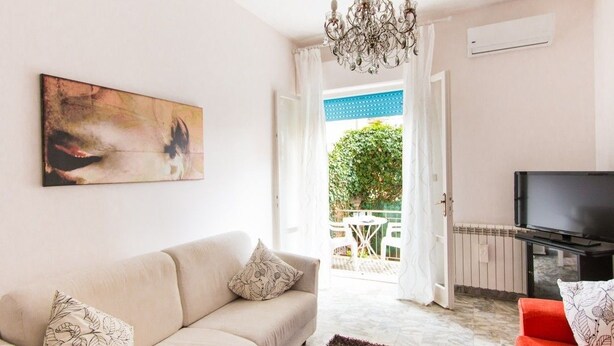 A living room with a beige sofa, a red sofa, a chandelier, a television, and a painting on the wall. - Acquadimare (Viareggio)