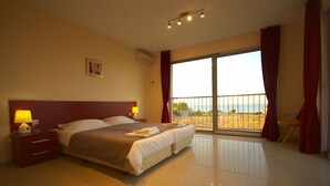 A large bed with two pillows, a nightstand with a lamp, and a chair near a sliding glass door with a view of the outdoors. - Seagarden Villa Resort (Tsarevo)