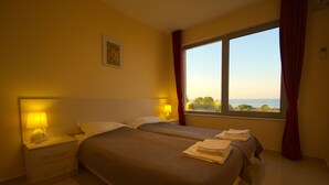 A hotel room with two beds, a nightstand with a lamp, and a window with curtains. - Seagarden Villa Resort (Tsarevo)