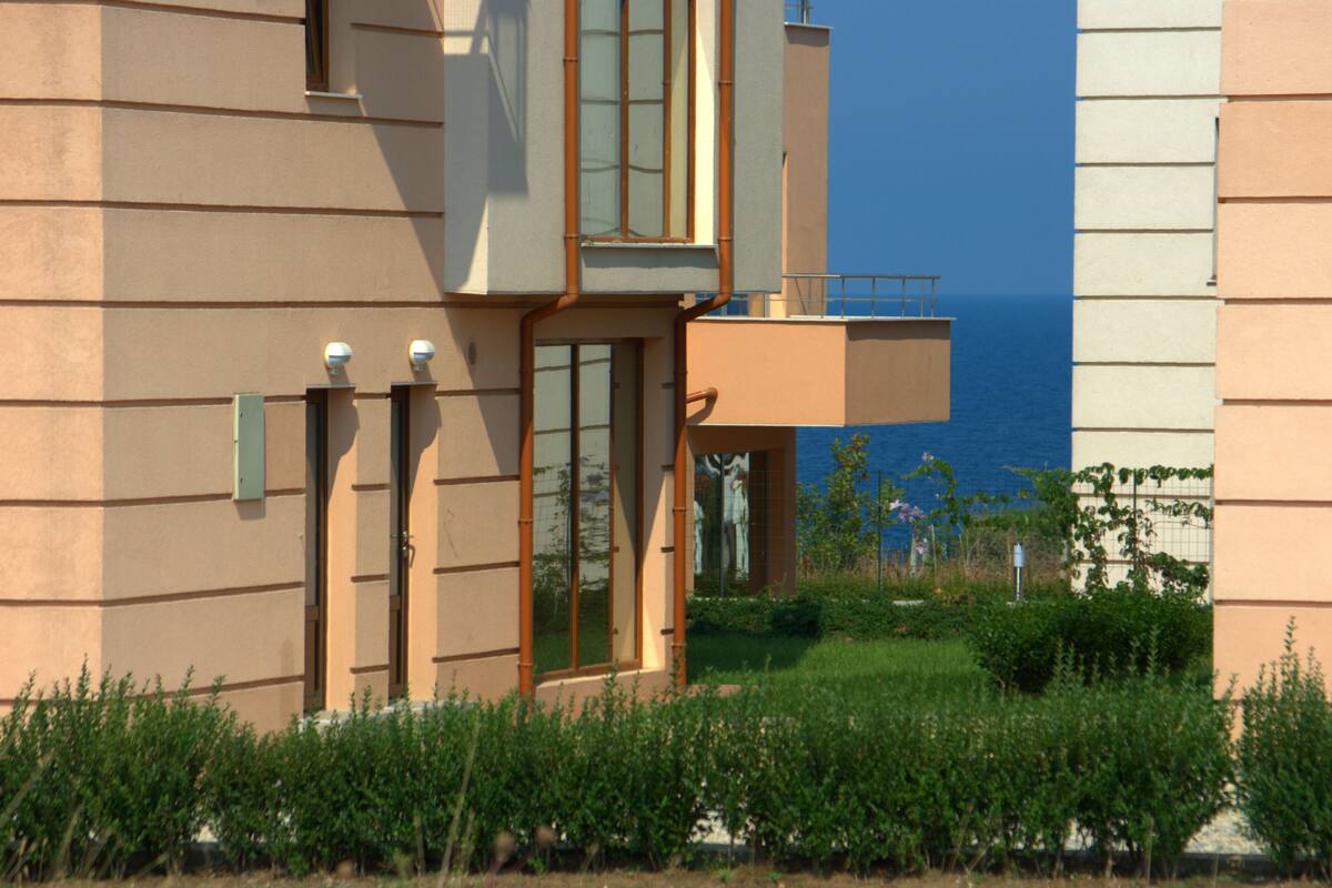 A modern building with a glass door, a balcony, and a view of the sea.