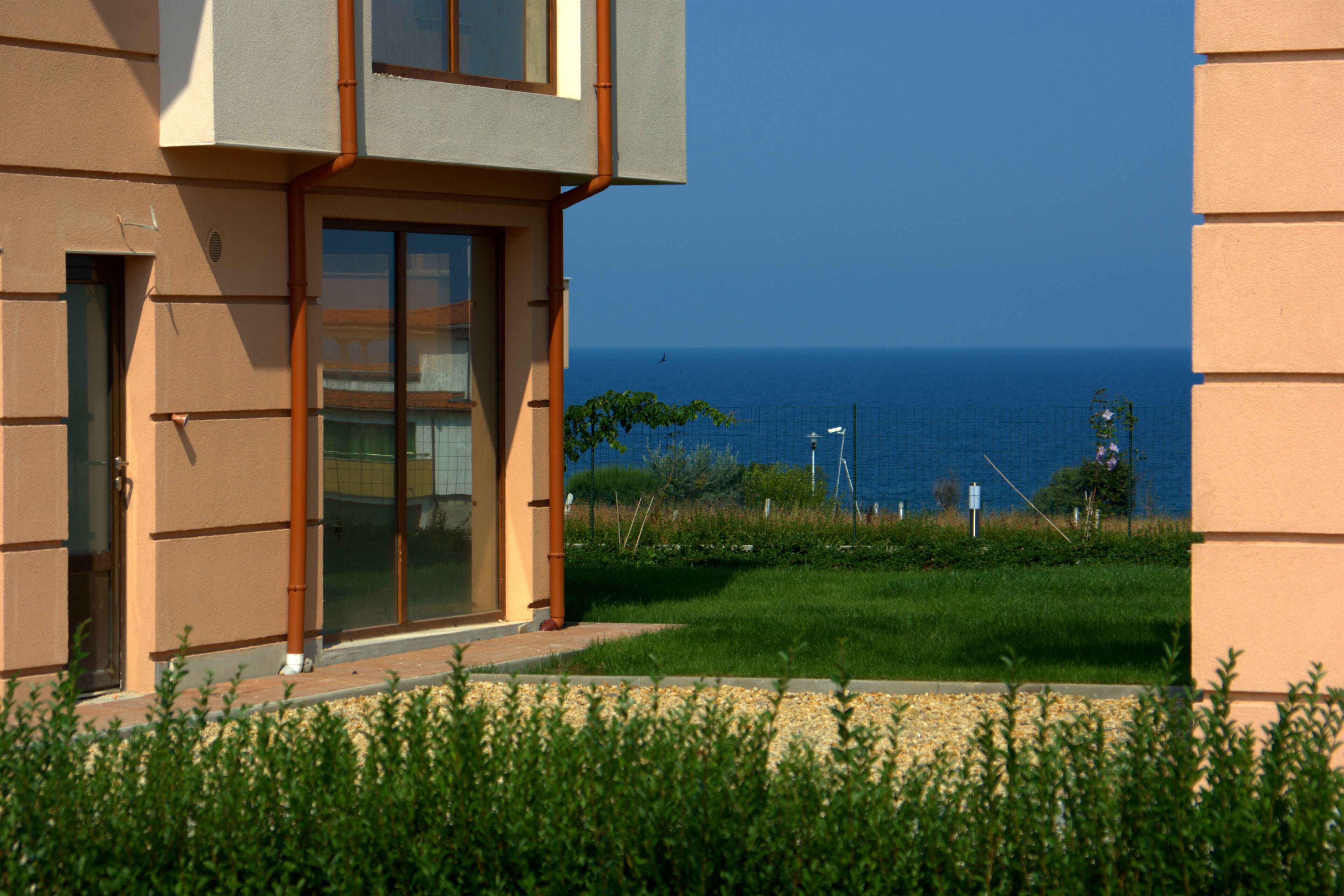 Ein modernes Gebäude mit Glastür und -fenstern, einer grünen Rasenfläche und Blick aufs Meer.
