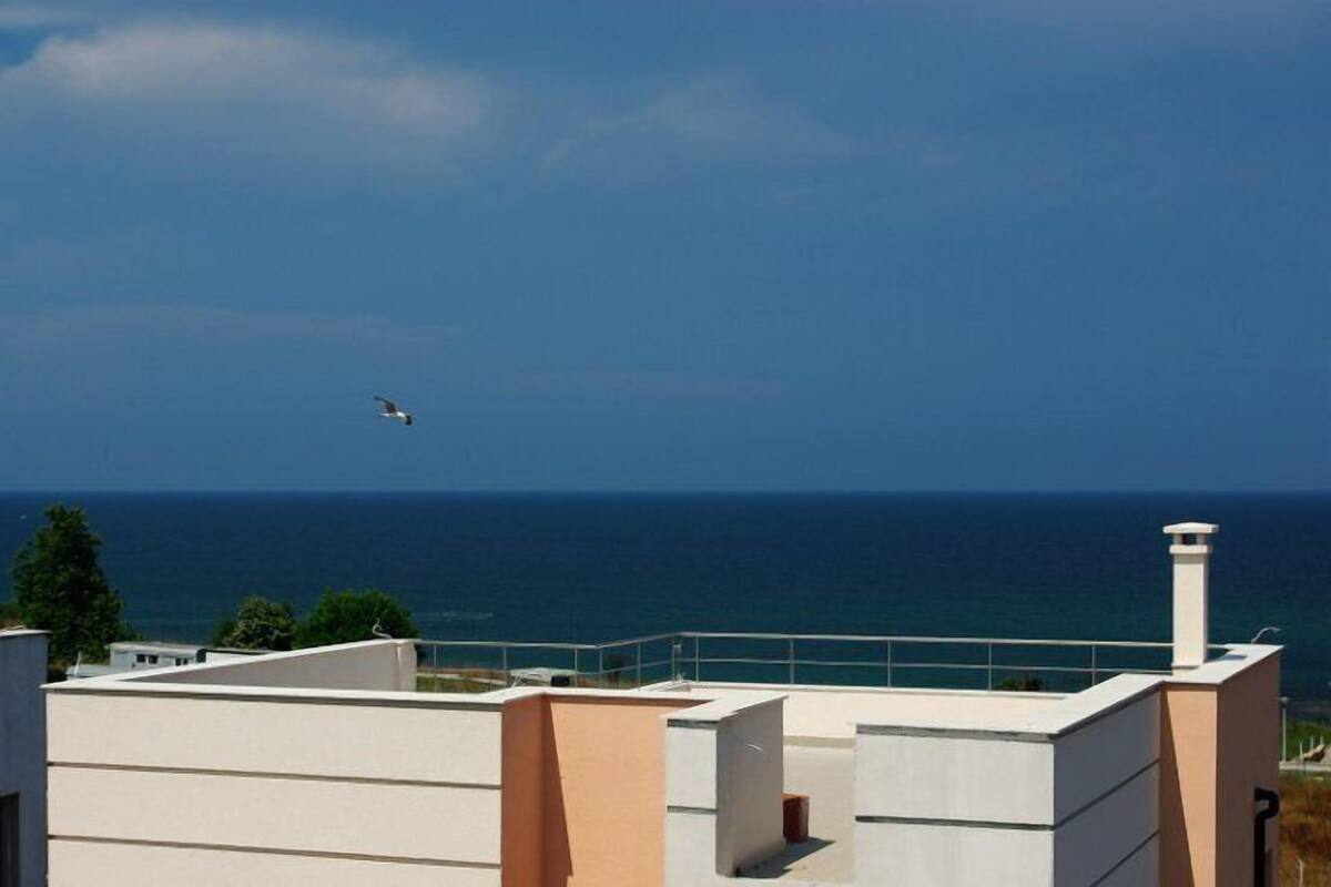 A modern building with a flat roof, a chimney, and a view of the sea.