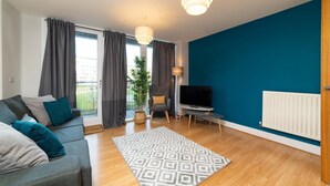 Un salon moderne avec un canapé gris, un tapis à motifs, un téléviseur et une grande fenêtre avec des rideaux.