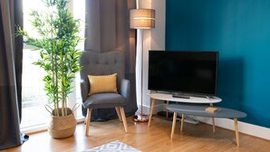 Un salon moderne avec un fauteuil gris, un téléviseur à écran plat, une lampe sur pied et une plante en pot.