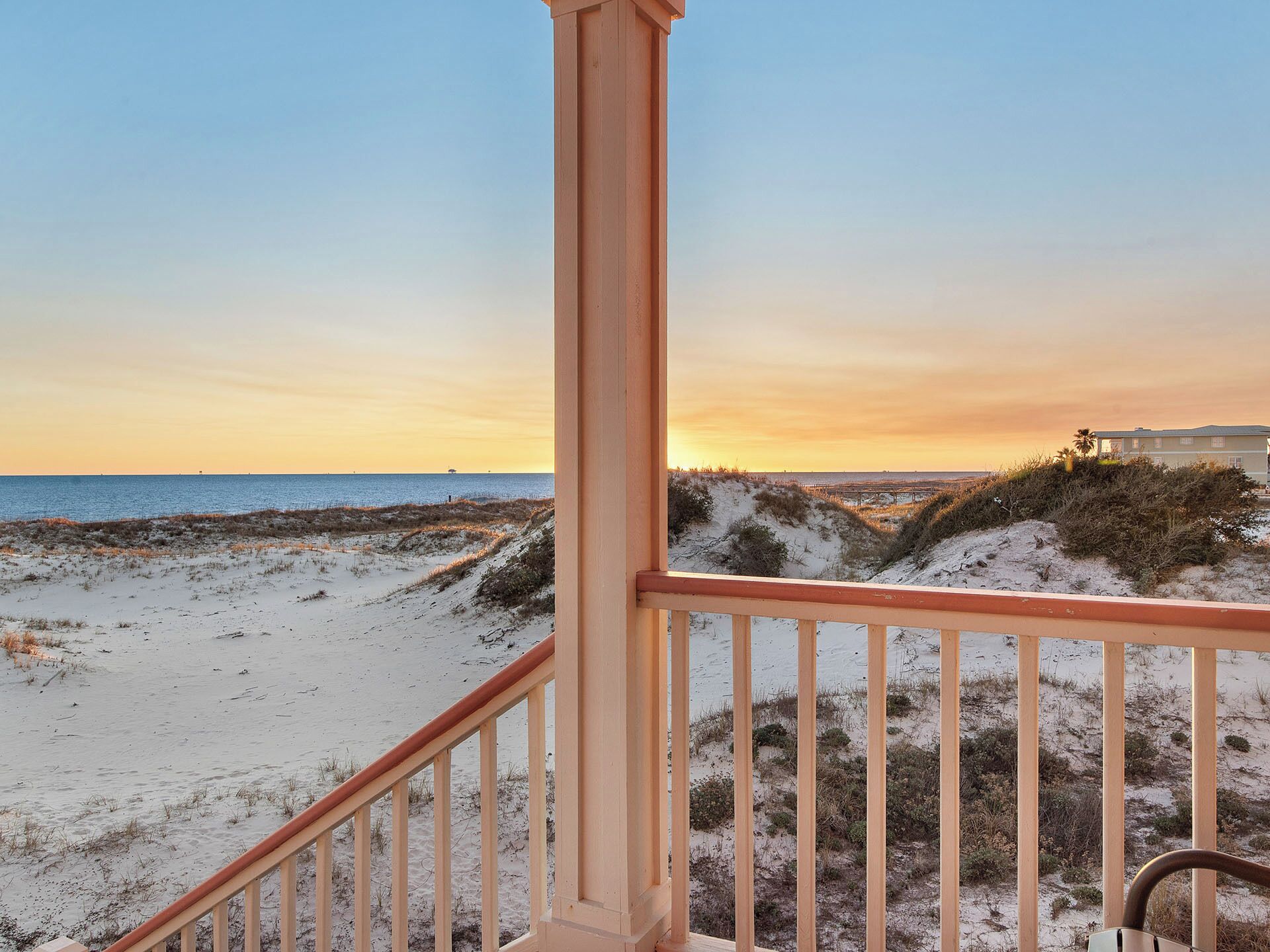 Vista sulla spiaggia da un balcone con ringhiera, dune sabbiose e un edificio in lontananza.