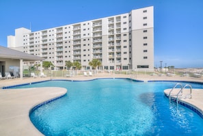 Un hotel con piscina, varios balcones y un cielo azul despejado.