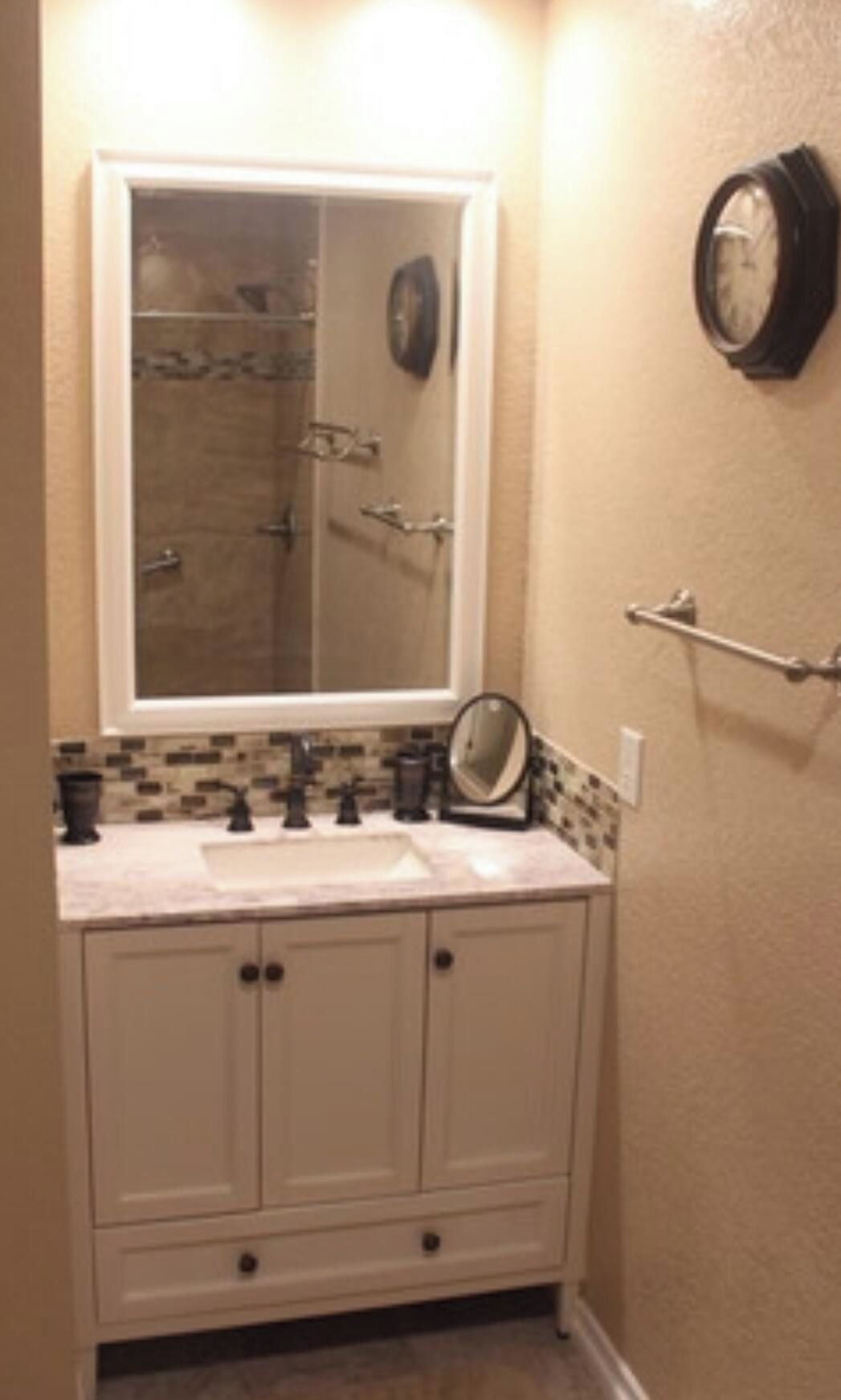 A bathroom with a white vanity, a mirror, a towel rack, and a shower visible through a glass door.