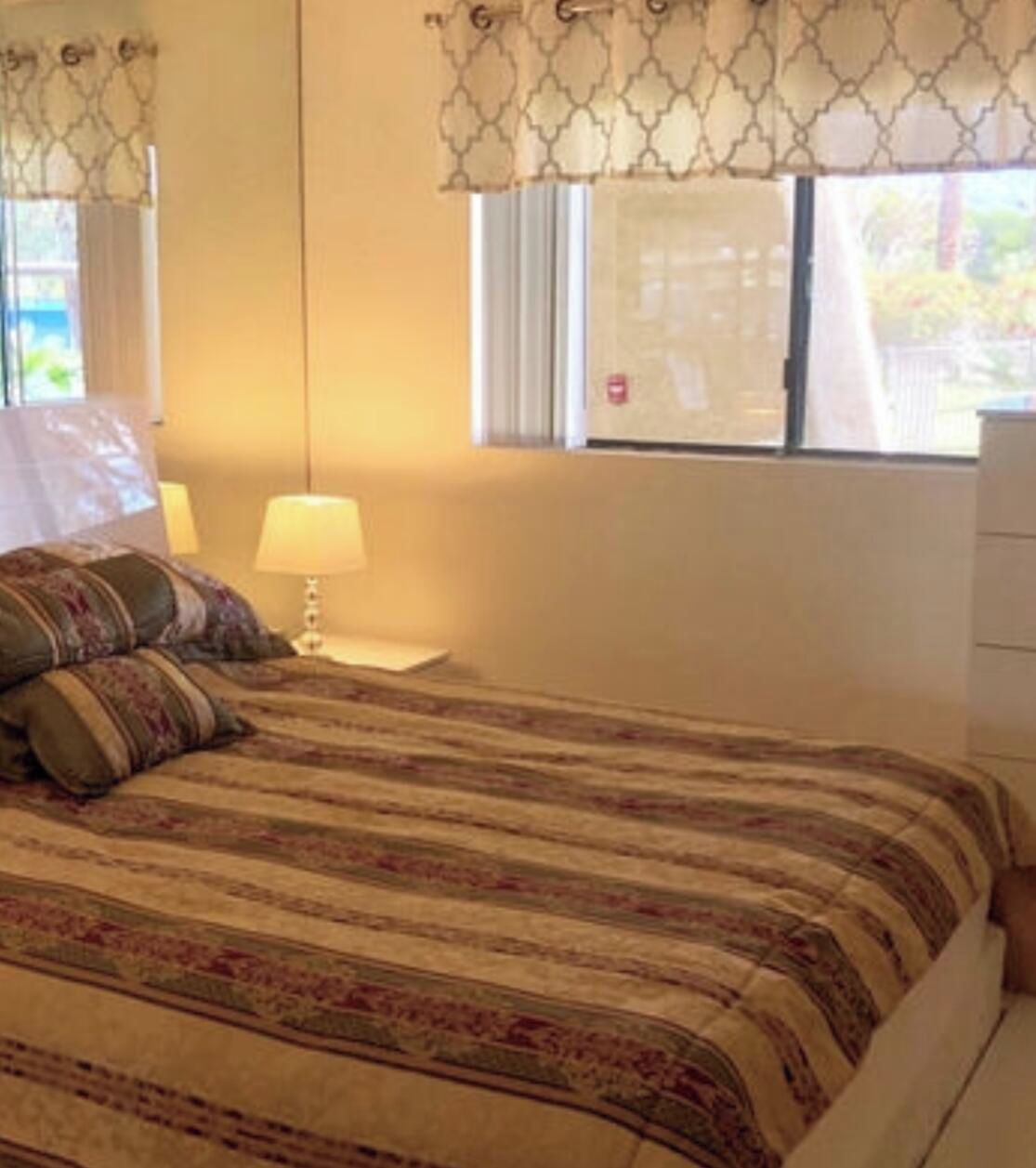 A bed with a patterned bedspread, a bedside lamp, and a window with a curtain.