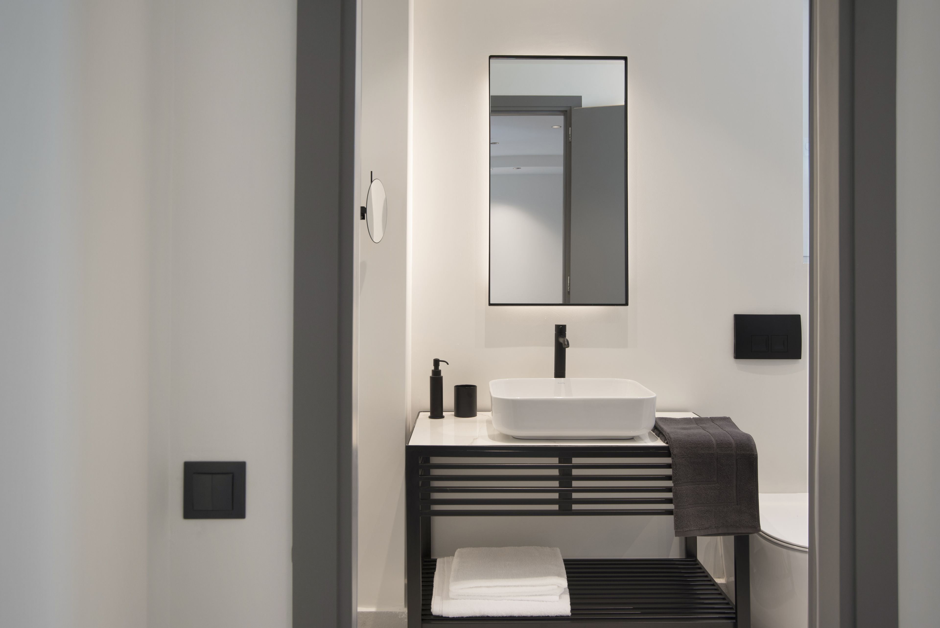 Un baño moderno con un lavamanos blanco, un espejo y un perchero para toallas.