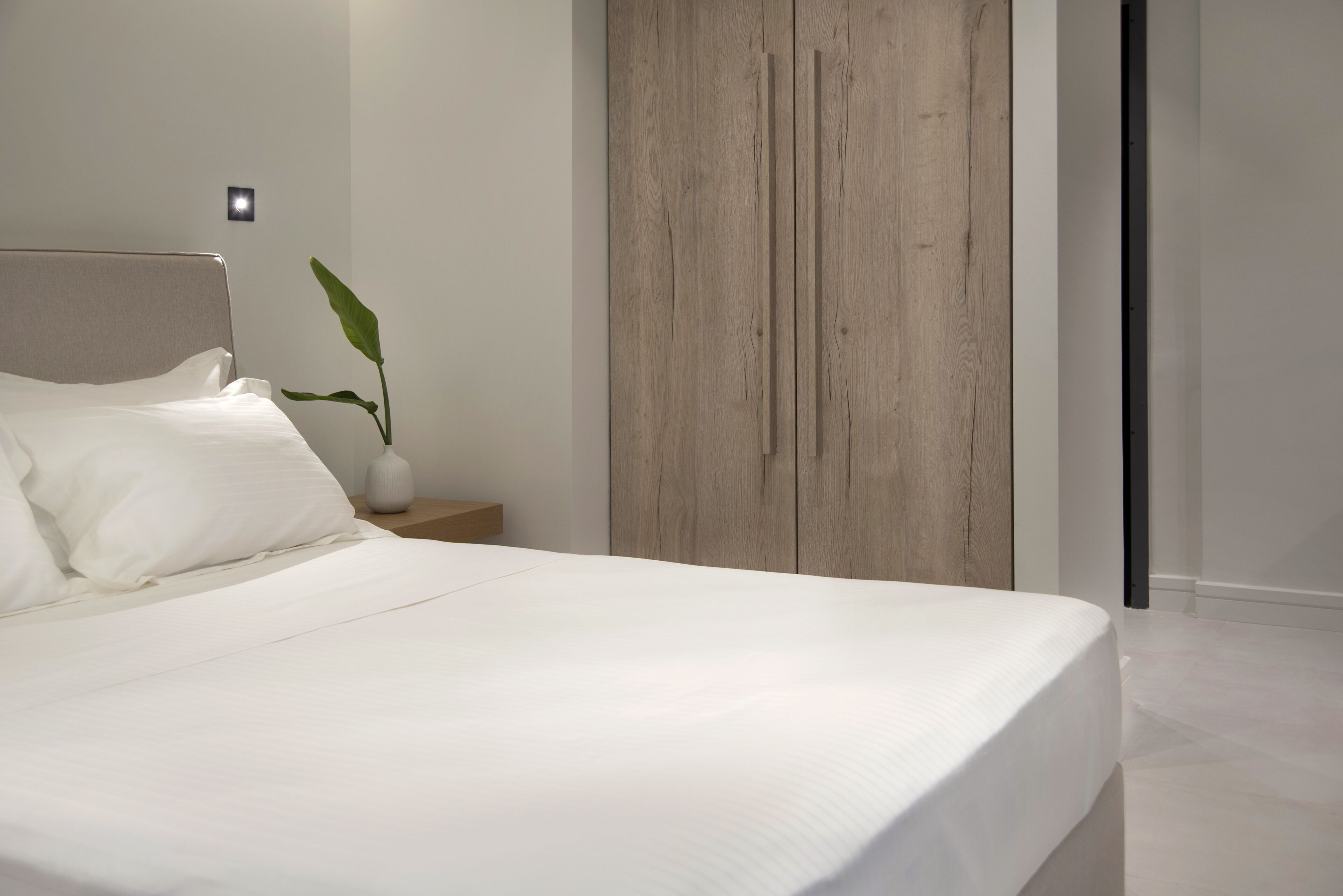 A modern bedroom with a large bed, a wooden wardrobe, and a bedside plant.