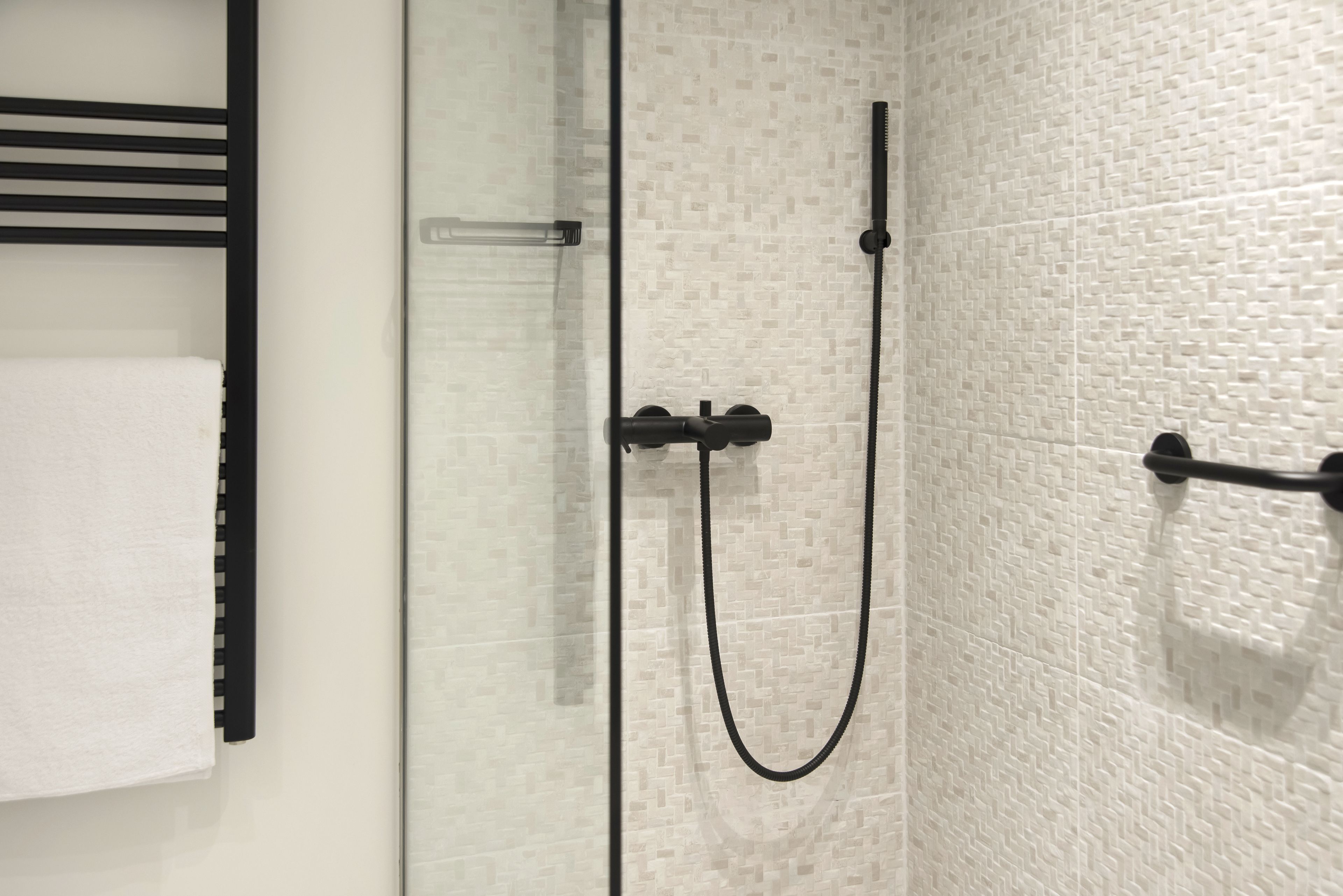 Eine begehbare Dusche mit Glaswänden, einem schwarzen Duschschlauch und einem Handtuchhalter mit einem weißen Handtuch.