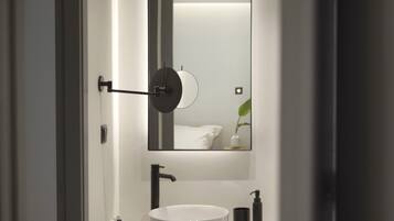 A modern bathroom with a round white sink, a black faucet, a mirror, and a wall-mounted towel rack.