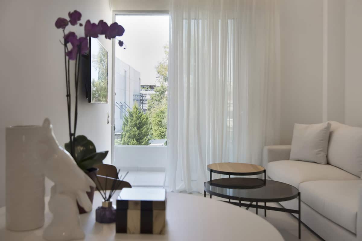 A modern living room with a white sofa, a round coffee table, and a view of greenery outside.