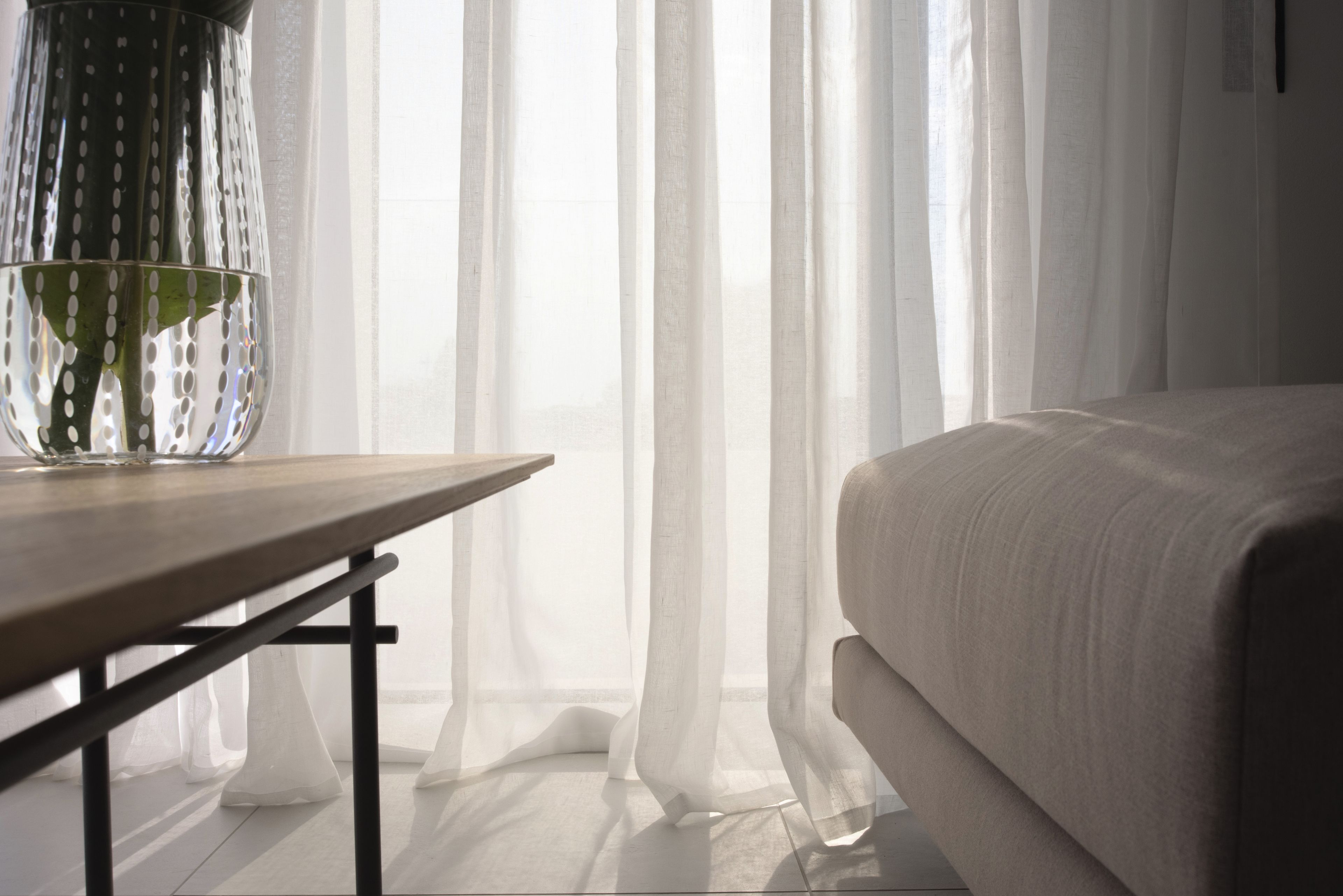 A bedroom with a bed, a wooden nightstand, and sheer curtains.