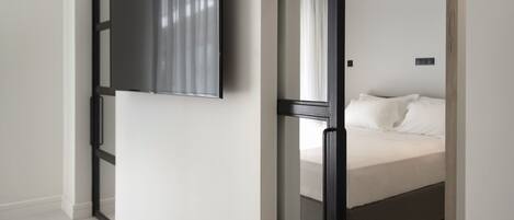A bedroom with a bed, a TV mounted on the wall, and a ceiling fan.