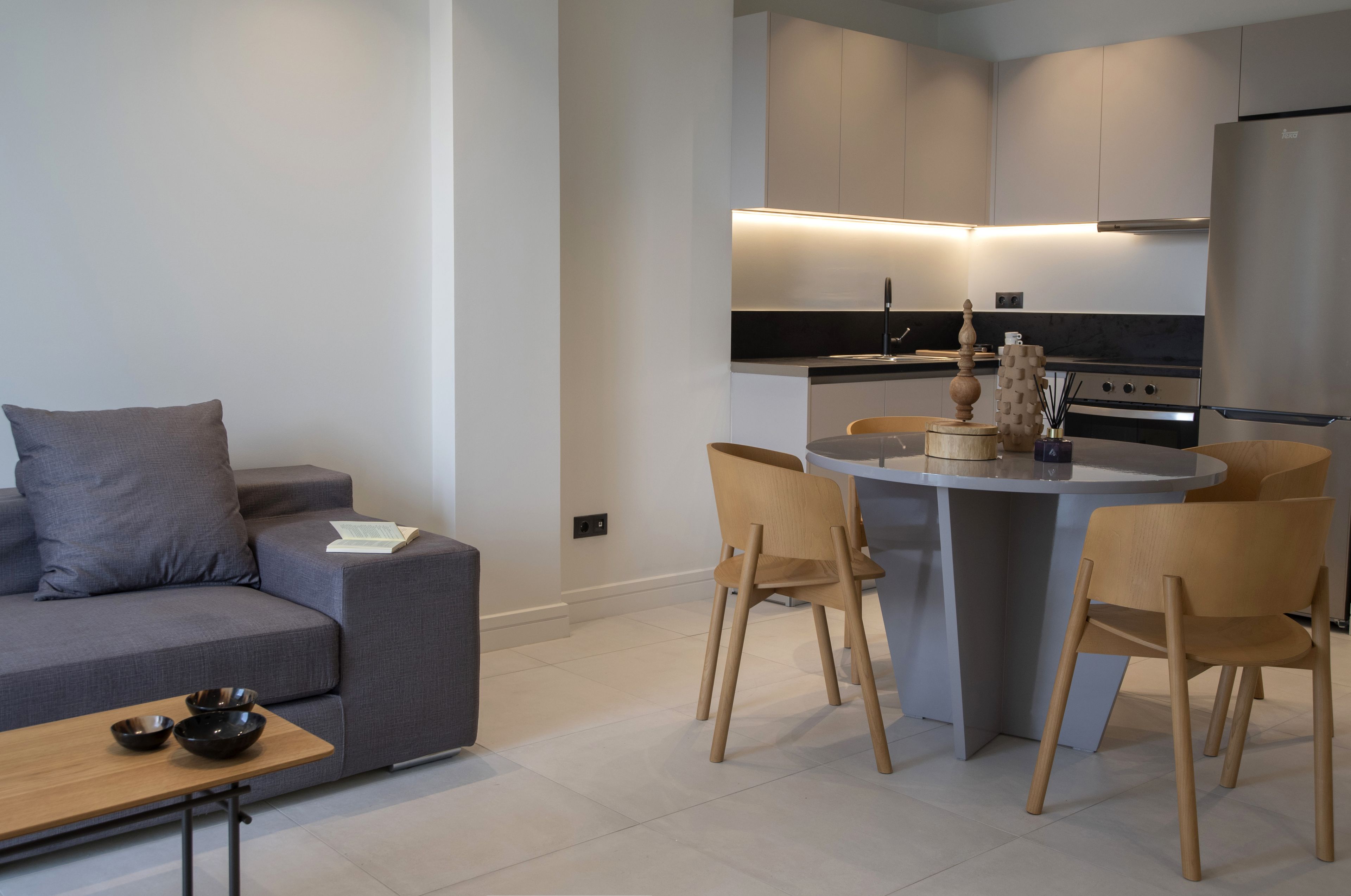 Une cuisine moderne avec un coin repas, un canapé gris et des chaises en bois.