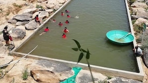 Ein rechteckiger Pool, umgeben von Felsen, mit Personen im Wasser und einem grünen Boot.