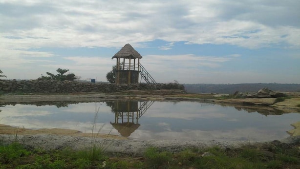 Ein Gebäude mit einem Strohdach und einer Treppe, die davor führt, neben ruhigem Wasser mit Spiegelung.