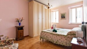 Une chambre à coucher comprenant un lit, une armoire, une table de chevet, une chaise et une fenêtre.