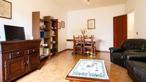 Un salon comprenant un meuble en bois, un téléviseur, une bibliothèque, une table à manger avec des chaises et un canapé en cuir noir.