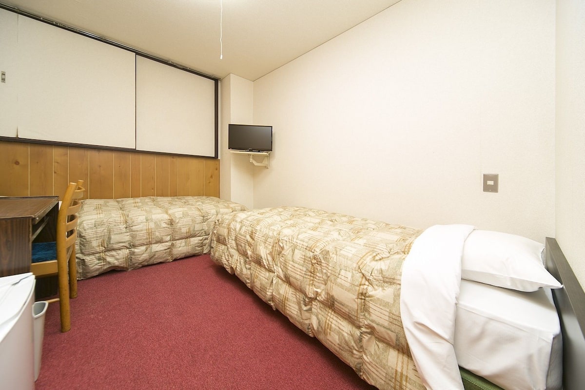 Una habitación pequeña con una cama individual, cabecera de madera, escritorio y televisor instalado en la pared.