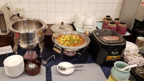 Montaje de bufé con diversos platos y recipientes, incluyendo una cocedora de arroz, una olla grande y varias botellas de salsas.