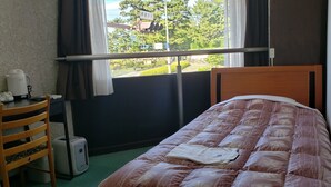 Un dormitorio con cama, una silla, un hervidor y una ventana que ofrece vistas a árboles y edificios.