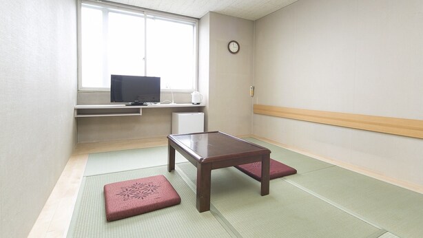 Una habitación con esteras de tatami, una mesa de madera, un televisor en una estantería y un reloj en la pared.