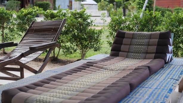 A sunbed with a patterned cover, a wooden lounge chair, and a small table with a checkered tablecloth. - Samui Caravans Hill Camp (Koh Samui)