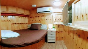 A wooden cabin room with a bed, a bedside table with a lamp, and an air conditioning unit. - Samui Caravans Hill Camp (Koh Samui)