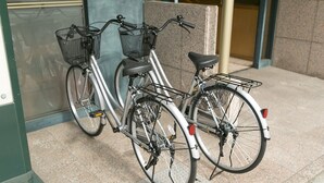 To cykler parkeret på flisebelagte område nær en bygningseingang.