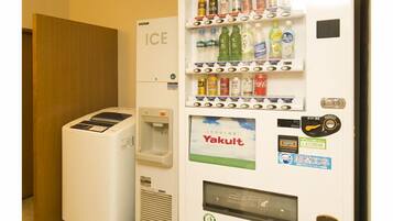 Ein Getränkeautomat mit einer Auswahl an Getränken und ein kleiner Kühlschrank mit der Aufschrift 'ICE' daneben.