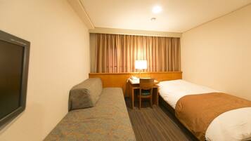 Habitación de hotel con una cama individual, un escritorio con silla, televisión y ventana con cortinas.