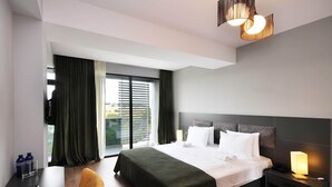 Une chambre d’hôtel moderne, dotée d’un grand lit, d’un bureau, d’une chaise, d’une table de chevet avec une lampe et offrant une vue sur l’extérieur par la fenêtre.