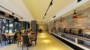 Un espace de restauration moderne avec des tables et des chaises en bois, un buffet où les plats sont présentés, et de grandes fenêtres offrant une vue panoramique.