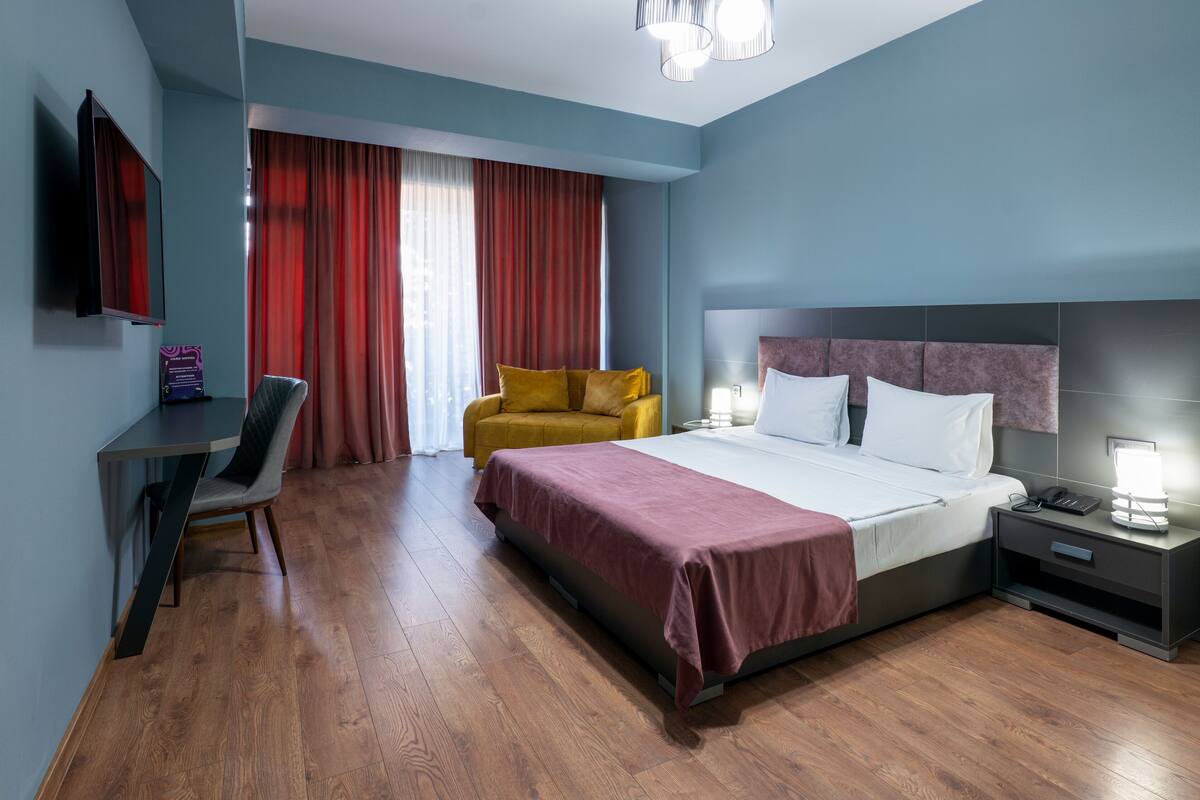 A modern hotel room with a bed, a desk, a chair, and a television.