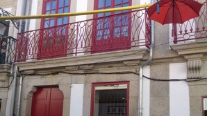 A building with red doors and windows, a balcony with red railings, and a colorful umbrella hanging above. - Hospedaria Nossa Senhora do Carmo (Viana do Castelo)