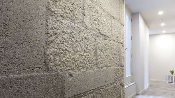 A hallway with a textured stone wall, wooden flooring, and recessed ceiling lights. - Hospedaria Nossa Senhora do Carmo (Viana do Castelo)