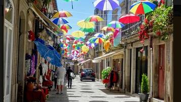 A narrow street with colorful umbrellas hanging overhead, shops on either side, and a car parked in the middle.