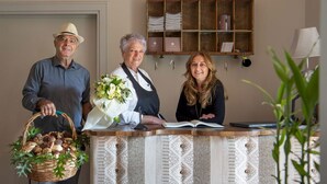 Een receptiebalie met een broodmand en bloemen, een houten plank met ordners en een lamp.